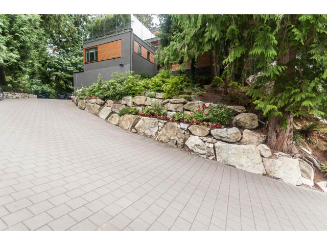Paved driveway leading to a modern house with stone landscaping and greenery. - 5385 Kew Cliff Rd, West Vancouver