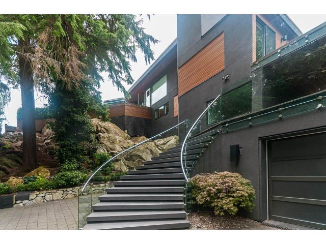 Modern 5-bedroom house with sleek black stairs and glass railings, surrounded by lush greenery. - 5385 Kew Cliff Rd, West Vancouver
