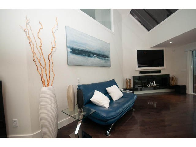 Spacious living room with blue leather sofa, modern art, and hardwood floors. - 5385 Kew Cliff Rd, West Vancouver