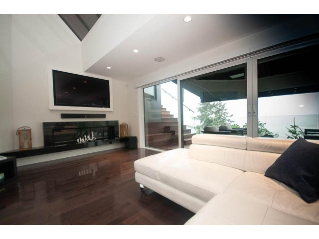 Bright living room with hardwood floors, modern fireplace, and large windows offering a city view. - 5385 Kew Cliff Rd, West Vancouver