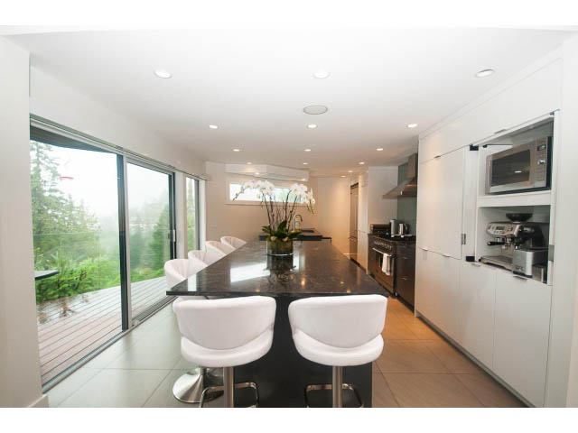 Bright kitchen with white cabinets, granite countertops, and a view of the deck. - 5385 Kew Cliff Rd, West Vancouver