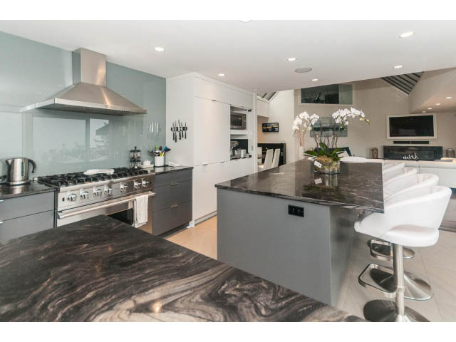 Bright kitchen with marble countertops and modern appliances, featuring a large island and bar stools. - 5385 Kew Cliff Rd, West Vancouver