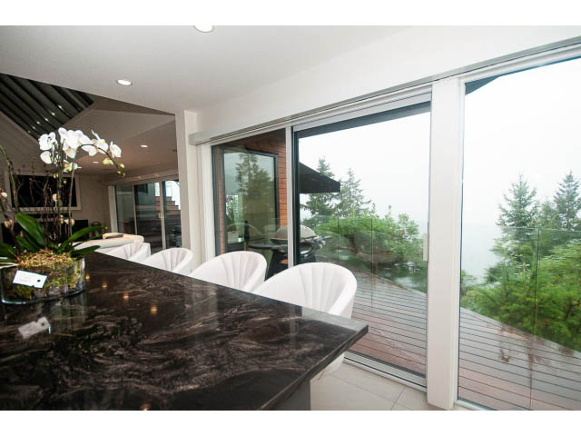 Bright kitchen with black granite countertops and large sliding glass doors leading to a deck with a city view. - 5385 Kew Cliff Rd, West Vancouver