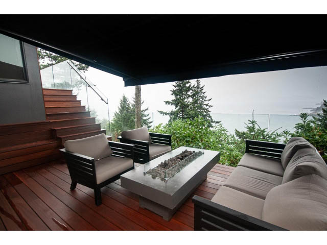 Furnished living room with modern furniture, wooden floors, and a scenic view of trees and water. - 5385 Kew Cliff Rd, West Vancouver