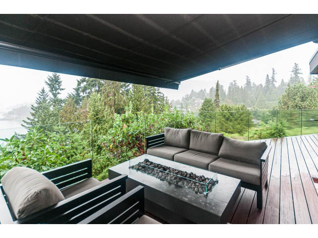 Furnished living room with outdoor fireplace, overlooking lush greenery and trees. - 5385 Kew Cliff Rd, West Vancouver
