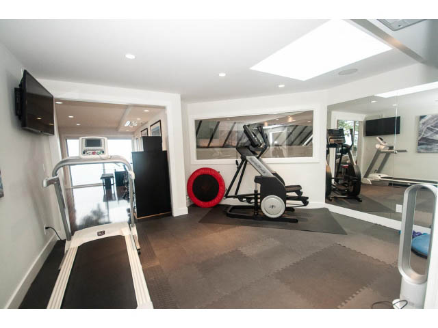 Bright gym with cardio equipment, mirrors, and a TV mounted on the wall. - 5385 Kew Cliff Rd, West Vancouver