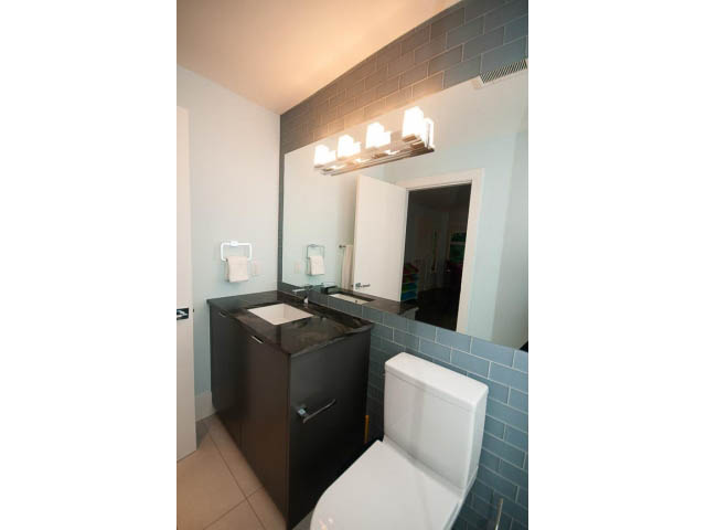 Bright bathroom with dark vanity, white toilet, and modern lighting fixture. - 5385 Kew Cliff Rd, West Vancouver