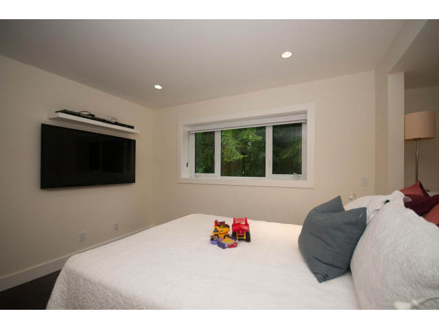 Bright bedroom with large window, modern TV, and neatly made bed. - 5385 Kew Cliff Rd, West Vancouver