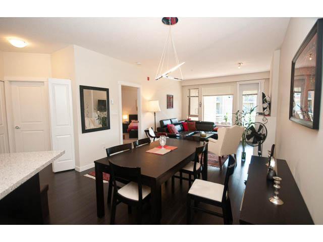 Furnished dining area with dark wood table, white chairs, and modern pendant lights. - 311 - 159 West 22nd Street, North Vancouver