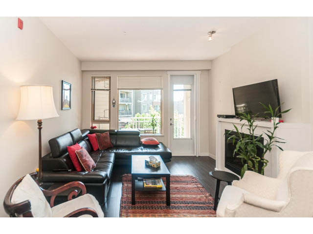 Furnished living room with black leather couches, wooden coffee table, and city view through large windows.