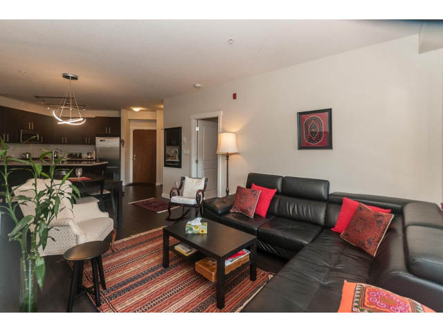 Furnished living room with black leather couch, colorful throw pillows, and a kitchen in the background. - 311 - 159 West 22nd Street, North Vancouver