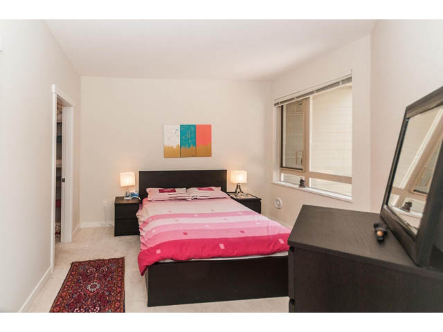 Bright bedroom with pink bedding and modern artwork, featuring a large window and a cozy rug. - 311 - 159 West 22nd Street, North Vancouver