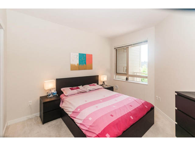 Bright bedroom with modern furnishings, pink bedding, and a sliding glass door leading to a balcony. - 311 - 159 West 22nd Street, North Vancouver