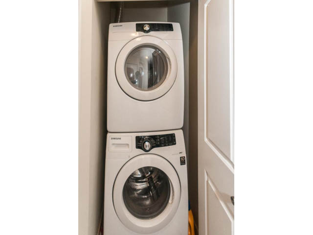 Bright laundry room with stacked washer and dryer, white cabinets. - 311 - 159 West 22nd Street, North Vancouver