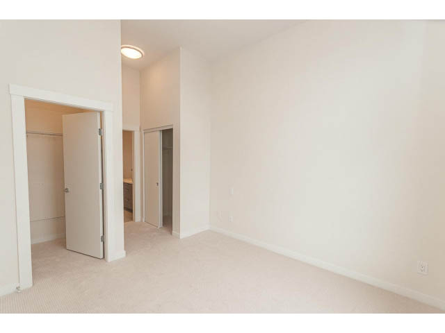 Bright living room with carpeted floor and white walls, leading to a den and another room. - 402 - 625 East 3rd Street, North Vancouver