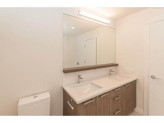 Bright bathroom with white fixtures and wood cabinets. - 402 - 625 East 3rd Street, North Vancouver