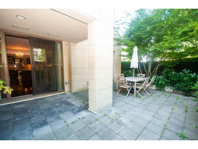 Furnished patio with outdoor seating and umbrella, surrounded by greenery. - 104 - 533  Waters Edge Cres, West Vancouver