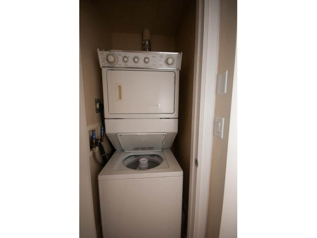 Bright laundry room with stacked washer and dryer, narrow hallway access. - 104 - 533  Waters Edge Cres, West Vancouver