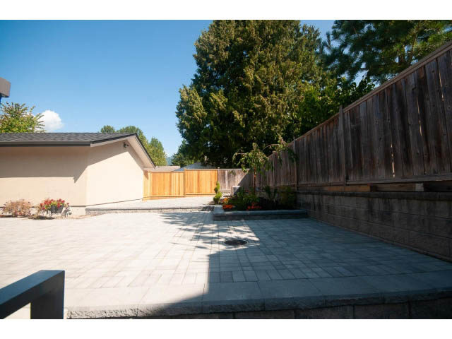 Bright patio with stone pavers and wooden deck, surrounded by trees and a neighboring house. - Suite - 430 West Windsor Road, North Vancouver