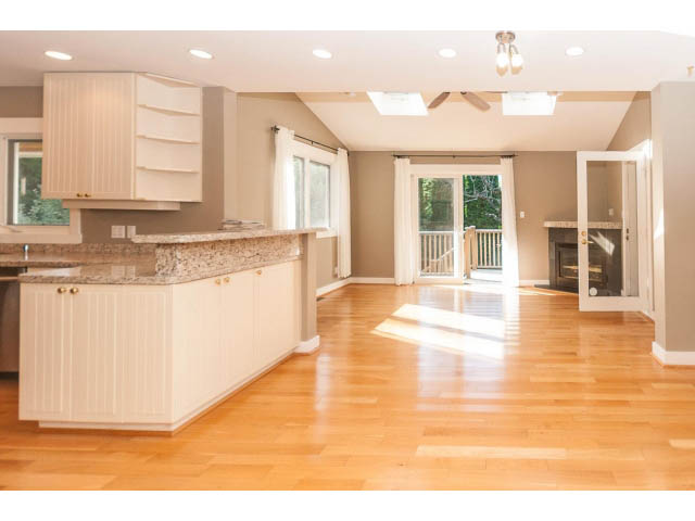 Bright kitchen with granite countertops and hardwood floors, leading to a spacious living area with large windows.