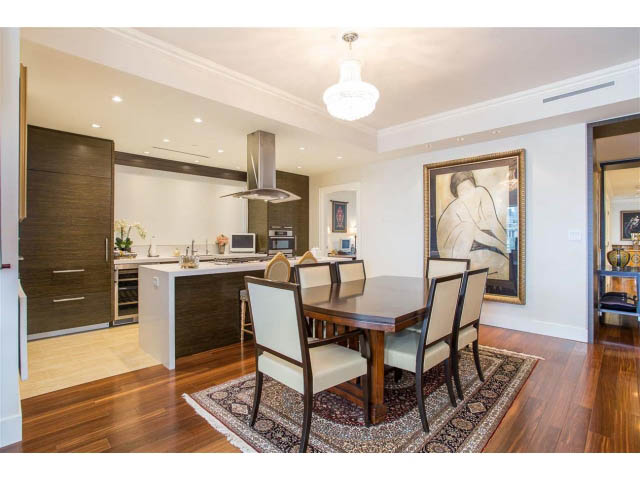 Furnished dining area with hardwood floors and a chandelier, leading to a modern kitchen with dark wood cabinets and...