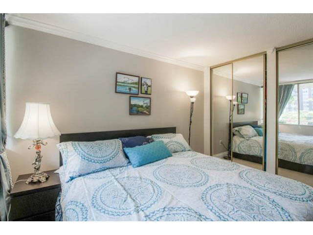 Furnished 2-bedroom bedroom with blue patterned bedding, wall art, and sliding glass doors. - 309 - 2008 Fullerton Avenue, North Vancouver