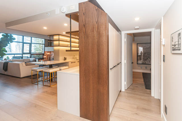 Bright kitchen with white countertops and hardwood floors, leading to a cozy living area with a city view.