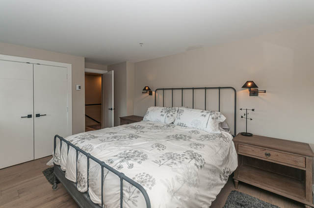 Spacious bedroom with wooden headboard and floral bedding, hardwood floors. - PH7 - 1688 Robson Street, Vancouver Downtown