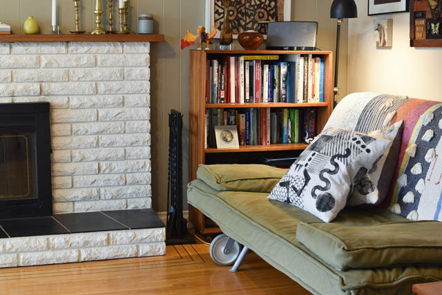 Furnished living room with a brick fireplace, hardwood floors, and a bookshelf. - 850 E 23rd Avenue, Vancouver East Side
