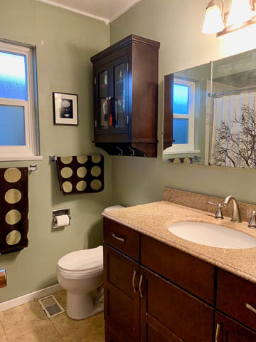 Bright bathroom with granite countertops and wooden cabinets, featuring a window view of the city. - 850 E 23rd Avenue, Vancouver East Side