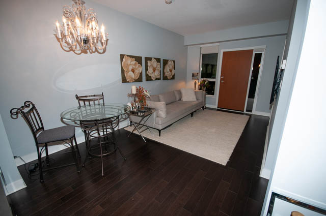 Furnished living room with hardwood floors and a dining area with a glass table. - 105 - 2020 W 12th Ave, Vancouver West Side
