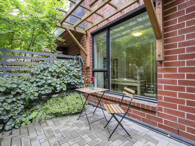 Furnished patio with brick walls, wooden furniture, and lush greenery. - 105 - 2020 W 12th Ave, Vancouver West Side