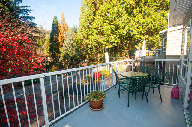 Furnished balcony with green chairs and tables, surrounded by trees and fall foliage. - 1528 Edgewater Lane, North Vancouver