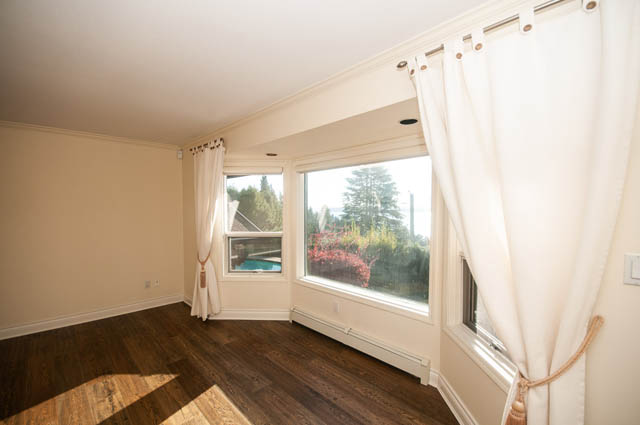 Bright living room with hardwood floors and large windows showing a view of trees. - 3399 Thompson Cres., West Vancouver