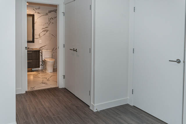 Bright hallway leading to a modern bathroom with marble walls and a toilet. - 404 - 733 E 3rd St, North Vancouver