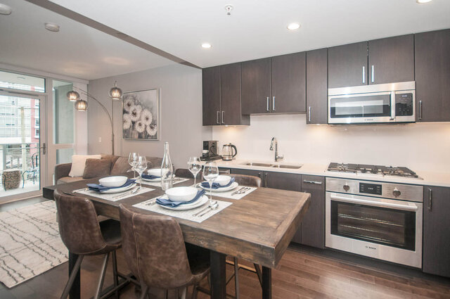 Modern kitchen with dark wood cabinets, stainless steel appliances, and a dining table set for four. - 401 - 1708 Ontario Street, Vancouver West Side