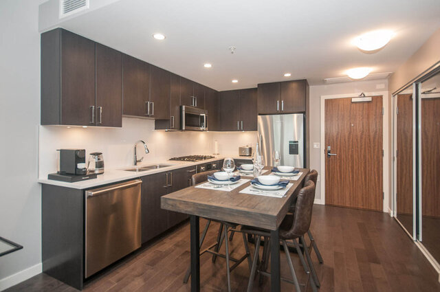 Modern kitchen with dark wood cabinets, stainless steel appliances, and a dining area with bar stools.
