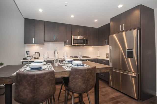 Modern kitchen with dark wood cabinets, stainless steel appliances, and a dining table set for four. - 401 - 1708 Ontario Street, Vancouver West Side