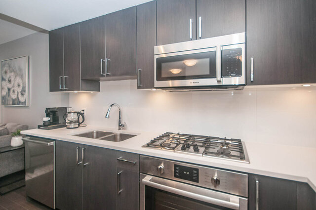 Bright kitchen with modern stainless steel appliances, dark wood cabinets, and white countertops. - 401 - 1708 Ontario Street, Vancouver West Side