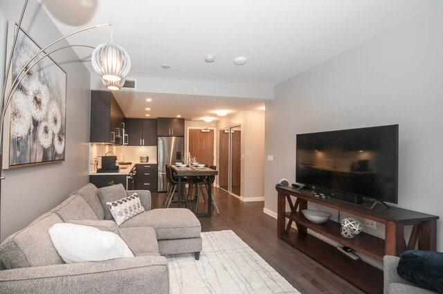 Spacious living room with modern furniture and a large flat-screen TV, featuring hardwood floors and a cozy ambiance.