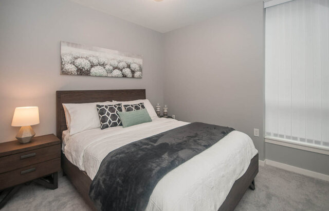 Spacious 1-bedroom + den condo with a cozy bedroom featuring a dark wood bed frame, white bedding, and a modern...
