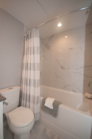 Modern bathroom with marble tiles and a striped shower curtain. - 401 - 1708 Ontario Street, Vancouver West Side