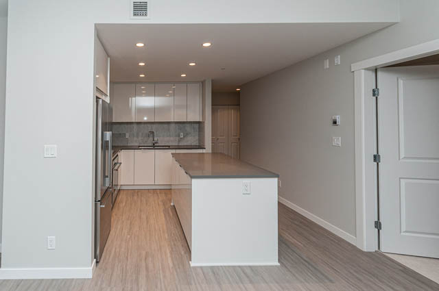 Bright kitchen with light wood cabinets, granite countertops, and hardwood floors. - 404 - 2632 Library Lane, North Vancouver