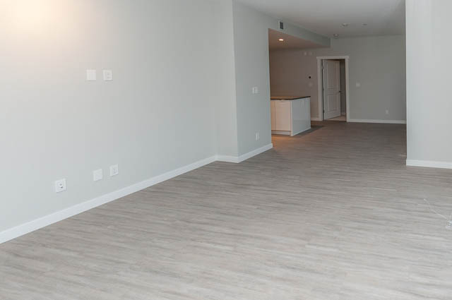 Bright living room with hardwood floors and kitchen in the background. - 404 - 2632 Library Lane, North Vancouver
