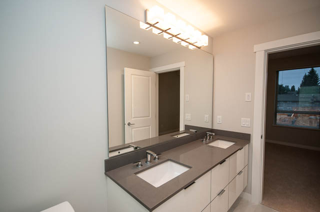 Bright bathroom with modern vanity and large mirror, city view through window. - 404 - 2632 Library Lane, North Vancouver