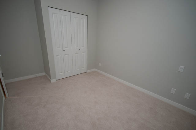 Empty bedroom with light carpet and white closet doors. - 404 - 2632 Library Lane, North Vancouver