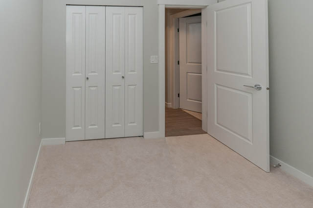 Bright hallway leading to three closed doors, light-colored walls, and a carpeted floor. - 404 - 2632 Library Lane, North Vancouver