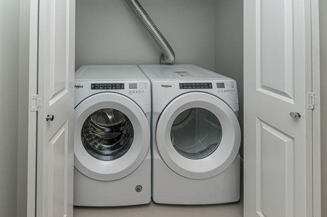 Bright laundry room with stacked washer and dryer, white cabinets. - 404 - 2632 Library Lane, North Vancouver