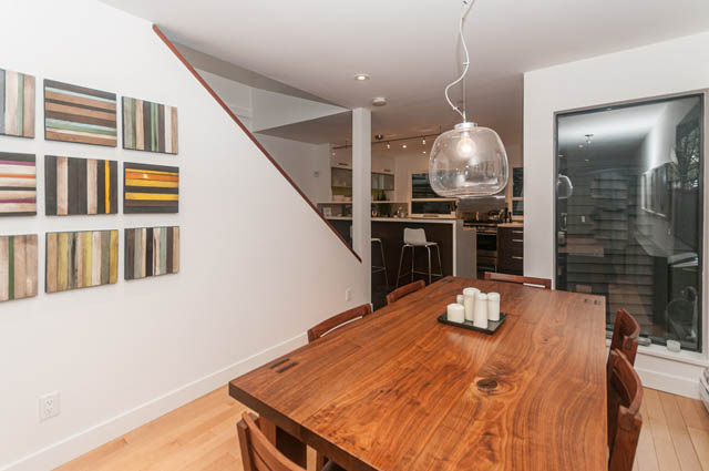 Furnished dining area with wooden table and chairs, leading to a modern kitchen with stainless steel appliances and...