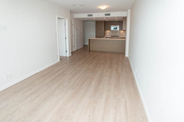 Bright living room with hardwood floors and kitchen in the background. - 1001 - 125 E 14th St, North Vancouver